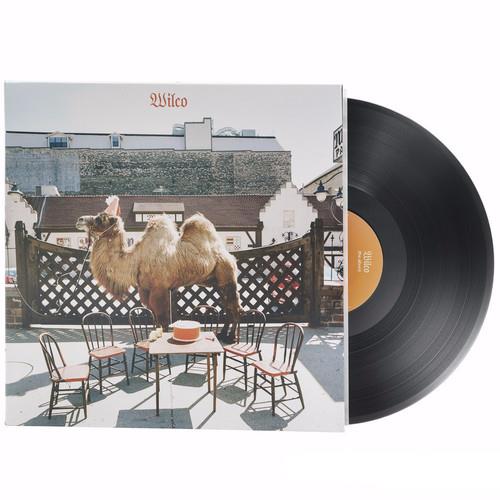 Vinyl record sleeve featuring a camel standing behind a table and chairs with a cityscape background