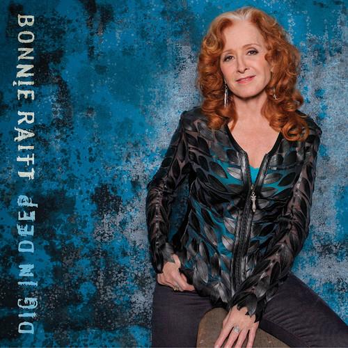Bonnie Raitt portrait with red hair wearing a black and teal patterned jacket against a blue texture