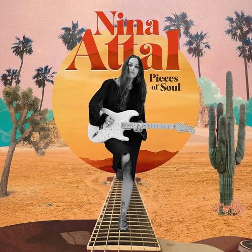 Woman in black holding a white electric guitar against a desert sunset backdrop with palm trees and