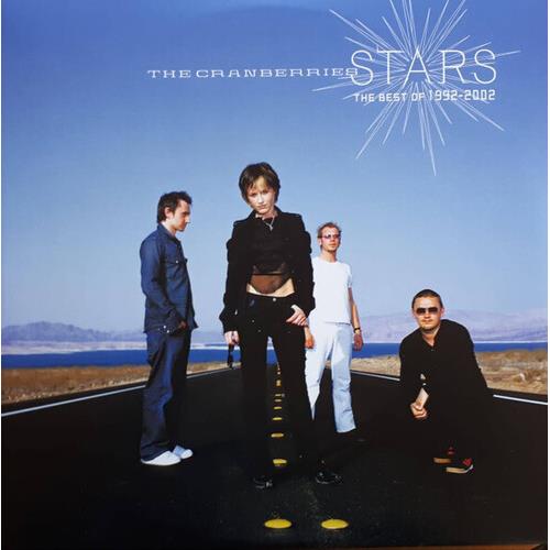 Four band members standing on a paved road against a blue sky and distant mountains