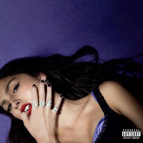 Woman with dark hair and red lipstick lying against a purple background with silver letter rings