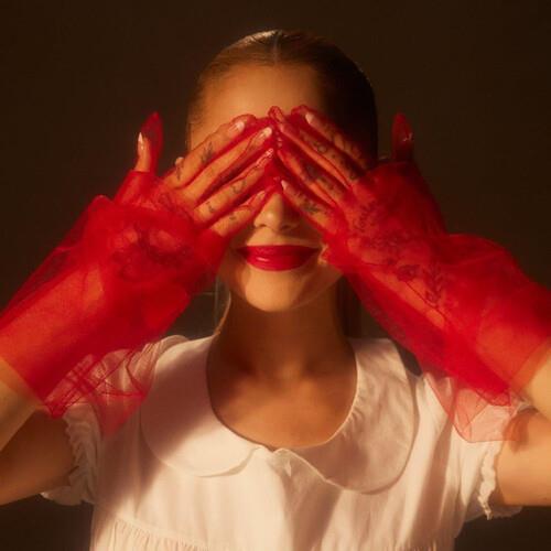 Woman in a white collared top wearing sheer red lace gloves covering her eyes