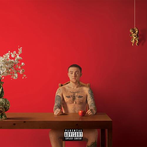 Shirtless man with tattoos seated at a wooden table with an apple