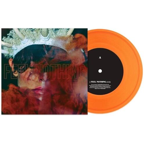 Translucent orange vinyl record with black center label next to album sleeve featuring a face with a