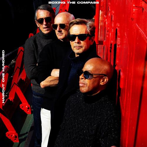 Four men in sunglasses and dark sweaters standing against a red wooden wall