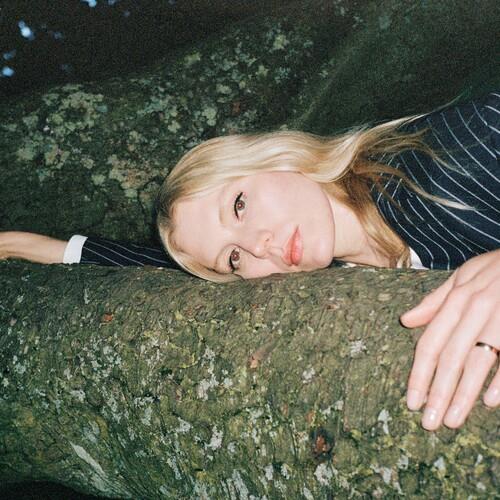 Blonde woman in a striped shirt resting her head on a tree branch