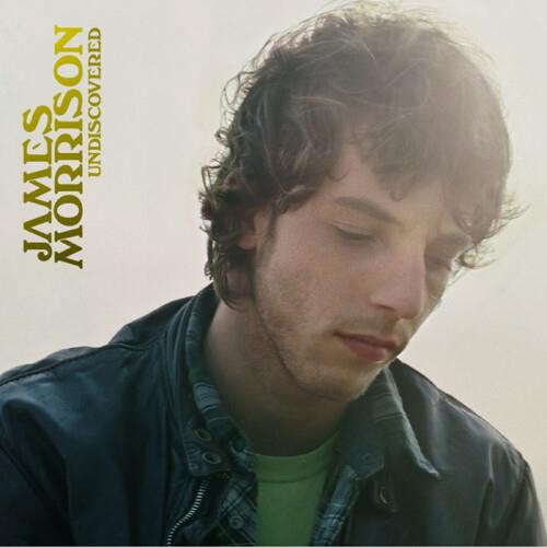 Portrait of a man with curly brown hair looking down, wearing a dark jacket over a green shirt