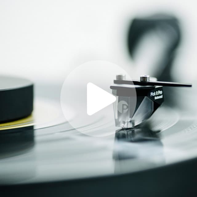 Black turntable cartridge with silver stylus tracking a vinyl record