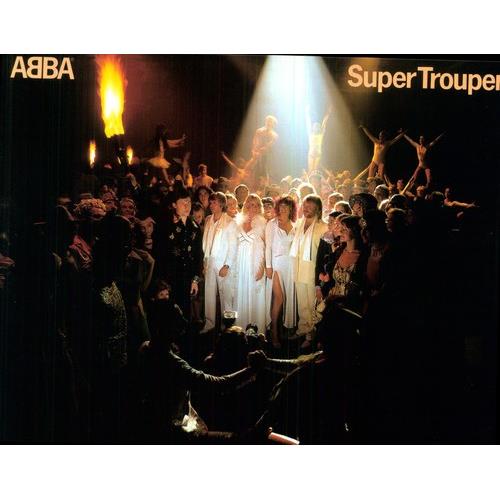 Four performers in white outfits surrounded by a crowd under a spotlight