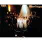 Four performers in white outfits surrounded by a crowd under a spotlight