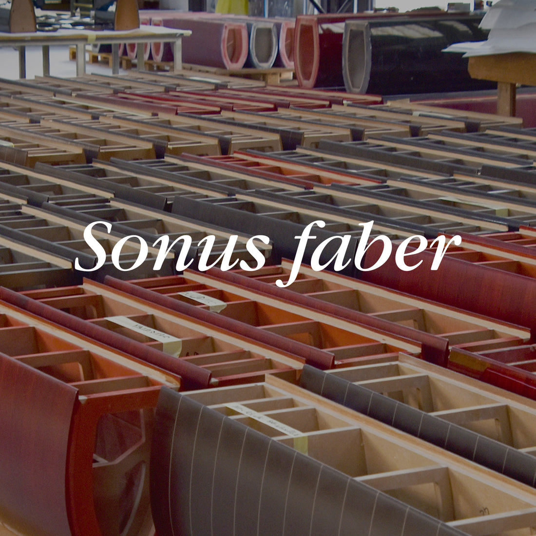 Rows of unfinished wooden speaker cabinets in red and black finishes on a factory floor