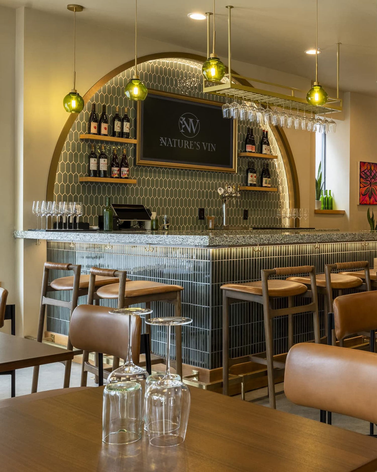 Modern wine bar with green hexagonal tile backsplash, wooden shelves, and brown leather bar stools Elegant wine bar with custom tilework, illuminated shelving, pendant lighting and counter seating in Wayne, PA