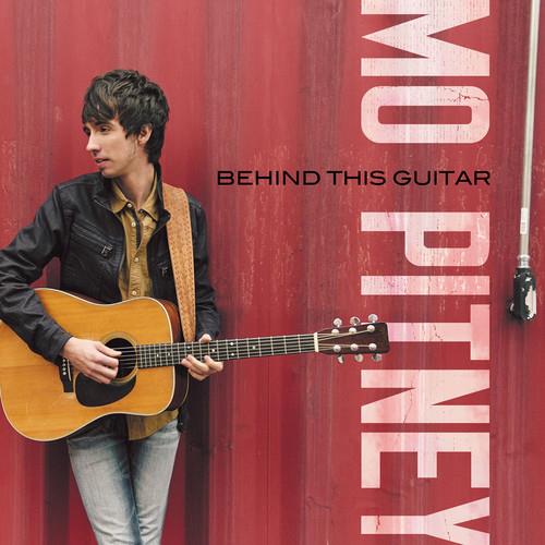 Man in black jacket holding acoustic guitar against red wall