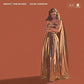 Woman in a gold metallic gown standing against a solid rust background