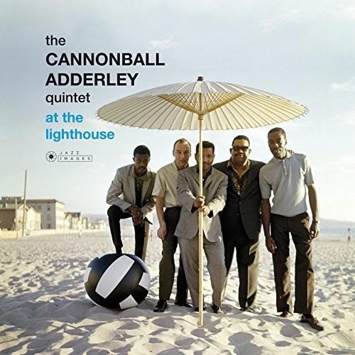 Five men in suits standing on a beach under a large parasol