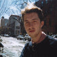 Portrait of a man on a snowy city street with bare trees and parked cars