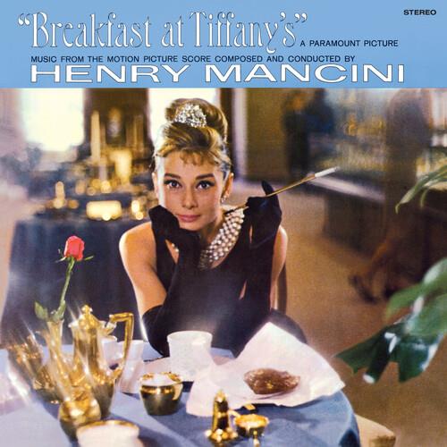 Woman in black dress and pearls holding a long cigarette holder at a cafe table