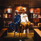 Two men in basketball jerseys seated on stools in a trophy room