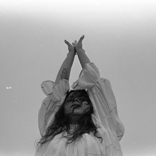 Black and white portrait of a woman with arms raised and hands clasped above her head
