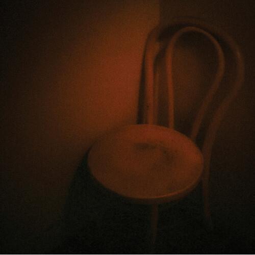 Dimly lit wooden chair with a curved backrest and round seat in a dark room