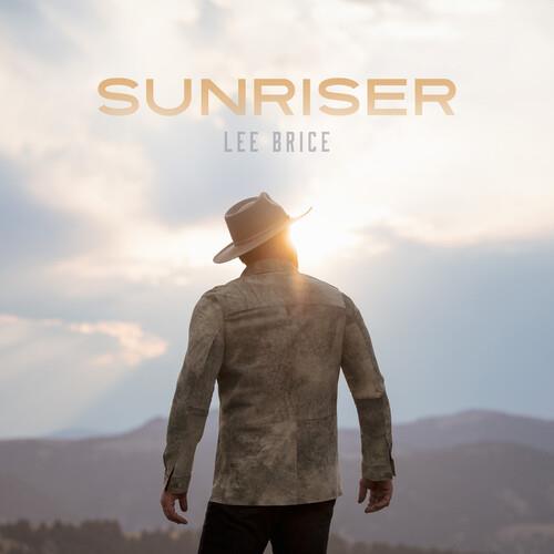 Man in a cowboy hat and suede jacket standing with his back to the camera against a sunset