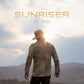 Man in a cowboy hat and suede jacket standing with his back to the camera against a sunset