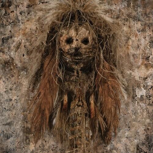 Mummified figure with hollow eyes and long fibrous hair against a textured wall