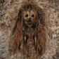 Mummified figure with hollow eyes and long fibrous hair against a textured wall