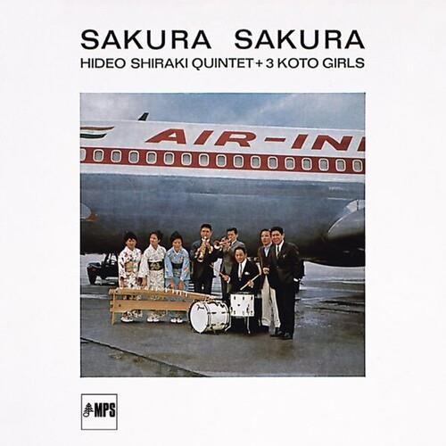 Jazz quintet and three women in kimonos posing with instruments in front of an Air India airplane