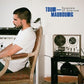 Man in white t-shirt seated in vintage armchair next to reel-to-reel tape recorder