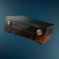 Black brushed metal AV receiver with a central display and dual control knobs